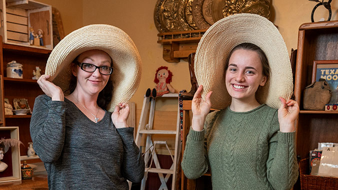 Two women smile for the camera in funny hats.